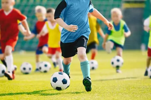 Kindersport Trainer - Fußball-Training für Kinder. Kinderfußballtraining. Kinder laufen und kicken Fußballbälle.