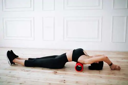Asiatische junge Frau, die Rückenmuskeln und Hüftmuskeln stärkt Bewegung mit Faszienmassagewalze auf dem Boden im klassischen Inneren.