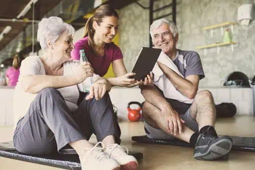 Fernstudium: Seniorentrainer - Senior Paar im Rehabilitationszentrum. Persönlicher Trainer, der etwas auf digitalen Tablets zeigt.