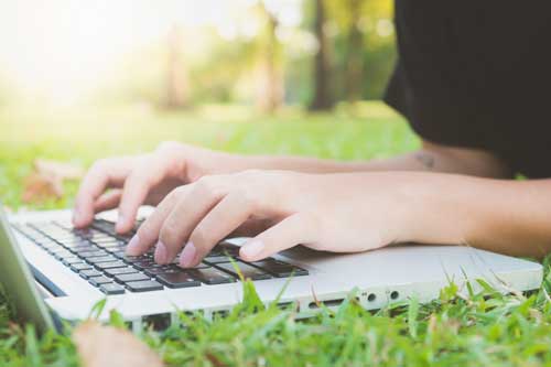 Sozialmanagement - Frau liegt im Gras und schreibt auf dem Laptop