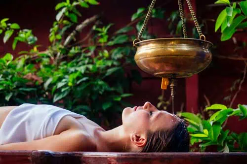 Fernlehrgang: Ayurvedische Diagnostik - Ayurveda Massage alternative Heiltherapie.Schönes, kaukasisches Weibchen, das eine Shirodhara-Behandlung erhält, liegt auf einem Holztisch im indischen Salon