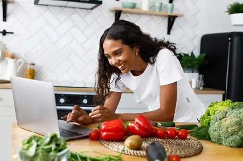 Food Coach - Frau am Laptop mit Obst und Gemüse im Hintergrund
