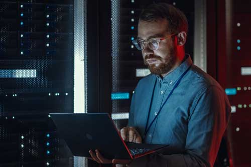 Netzwerkadministrator Microsoft Windows Server - Bearded IT Specialist in Glasses arbeitet am Laptop im Rechenzentrum, während es in der Nähe von Server Rack steht.