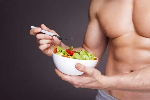 Sporternährung - Muskulöser Mann verzehrt Salat