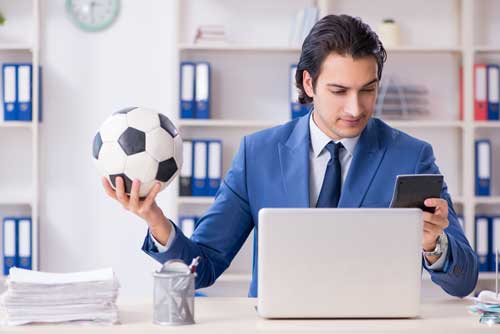 Spielerberater Fussball - Mann hält Ball in der Hand und arbeitet am Laptop
