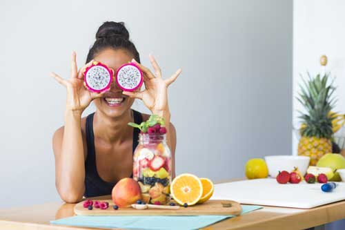 Ernährungsberater mit Fachrichtungen | Frau lächelt mit einem tropischen Fruchtsalat und spielt mit Drachenfrucht ihre Augen