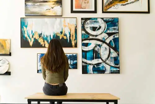 Junge weibliche Besucher, die auf einer Bank reflektieren und die verschiedenen Gemälde an der Wand einer Kunstgalerie bewundern