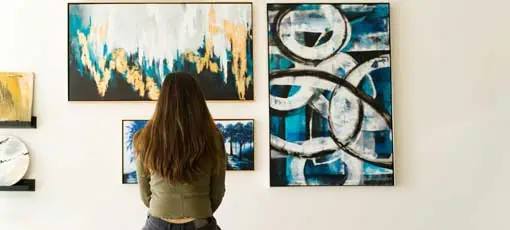 Junge weibliche Besucher, die auf einer Bank reflektieren und die verschiedenen Gemälde an der Wand einer Kunstgalerie bewundern