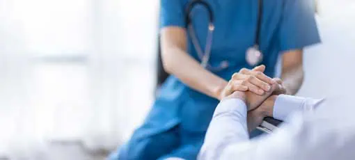Pflege Bachelor Fernstudium | Eine weibliche Krankenschwester, die sich in einer gepflanzten Aufnahme befindet, hält die Hand ihrer älteren Patientin. 