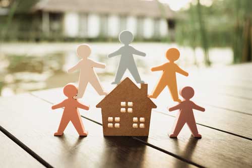Ausbildung Wohngruppenleiter | Modell eines Holzhauses und ein Modell von Menschen umgeben das Haus. Konzept der glücklichen Familie, Menschen leben und pflegen Häuser, Kauf, Hypotheken und Immobilien.