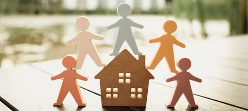 Ausbildung Wohngruppenleiter | Modell eines Holzhauses und ein Modell von Menschen umgeben das Haus. Konzept der glücklichen Familie, Menschen leben und pflegen Häuser, Kauf, Hypotheken und Immobilien.